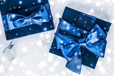 蓝色雪花摄影照片_冬季节日礼盒，配有蓝色丝绸蝴蝶结、大理石背景上的雪花，作为豪华美容品牌的圣诞和新年礼物，平铺设计