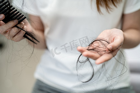 亚洲女性有长脱发问题，头发附着在梳子上。