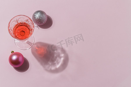 简约背景装饰图案摄影照片_粉红色背景的圣诞玩具的简约组合，玻璃杯里有鸡尾酒。