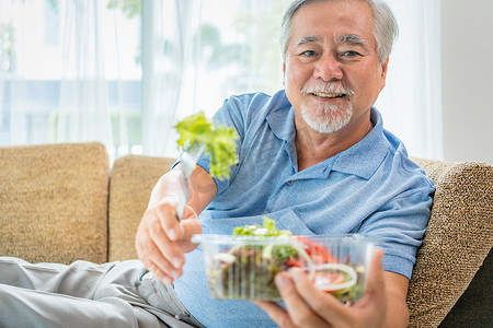 成熟男人用南瓜和健康食品，肖像亚洲老人在家里吃沙拉，老年男性保健吃蔬菜和有用的食物。