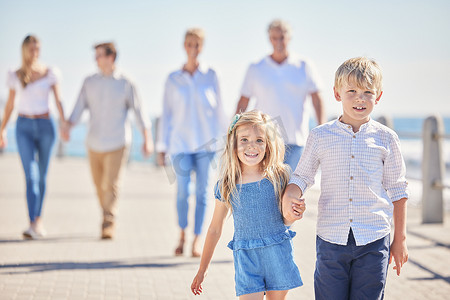 阳光明媚的日子里，可爱的弟弟妹妹手牵着手在海滨长廊上行走，而他们的父母和祖父母则跟在后面。