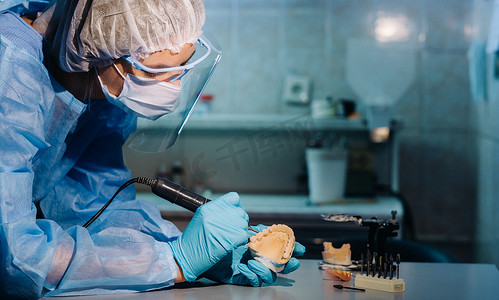 一位戴着面具和手套的牙科技师在他的实验室里制作假牙