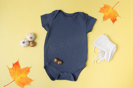 创意位置标志摄影照片_婴儿服装模型，黄色背景上有南瓜，适合秋季的文字或标志位置