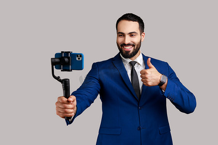 大胡子男博主拿着手机稳定器，制作视频或进行直播，竖起大拇指。