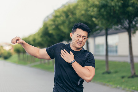男背摄影照片_亚洲男运动员，在公园里揉肩痛，手臂肌肉酸痛