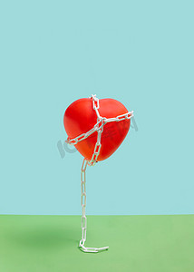 红色图案气球摄影照片_红色的心形与蓝色和绿色背景上的白色链条相连。