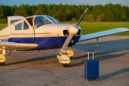 一个蓝色手提箱和一架已降落的小型私人飞机。