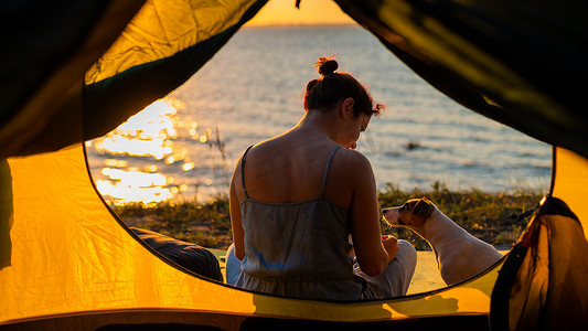 日落时分，女人和狗在旅游帐篷里。