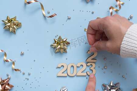 数字倒计时创意摄影照片_旧的 2022 年的数字已被新的 2023 年的数字所取代，在明亮的节日背景上有蝴蝶结和珠子