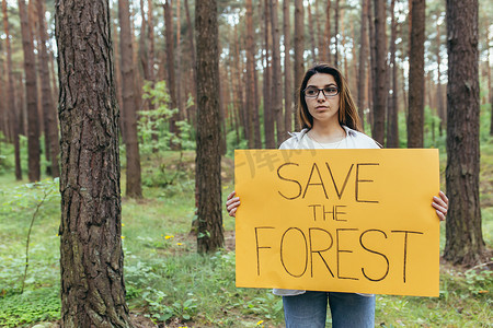 保护环境海报摄影照片_年轻女子在树林里做志愿者并举着拯救森林的海报
