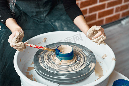 无法辨认的女人在轮子上制作陶瓷陶器，漆成蓝色。