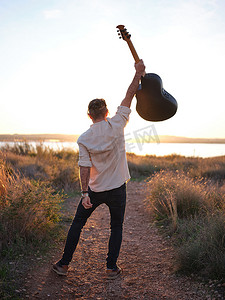 吉他手在湖边的日落前高举吉他