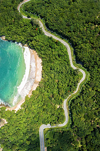 空中无人机自上而下地观看海浪在沙滩上与道路和森林的碰撞。