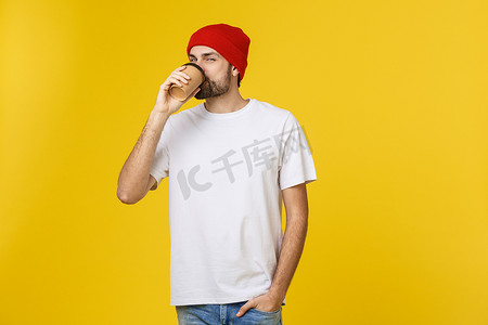 年轻的时髦男子拿着一杯咖啡，在黄​​色背景下被隔离。