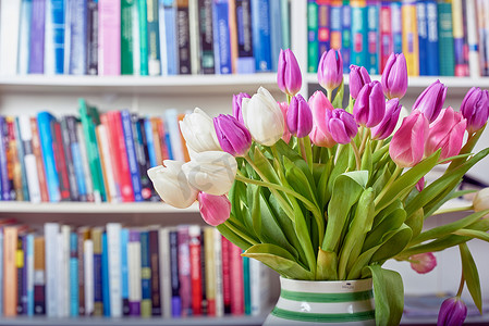 花瓶里放着新鲜的白色和粉色郁金香，背景是图书馆书架。