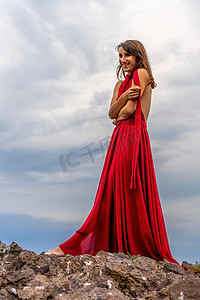 一名身着红色连衣裙的女子站在暴风雨的天空之上，她的裙子飘扬，布料在风中飘扬。