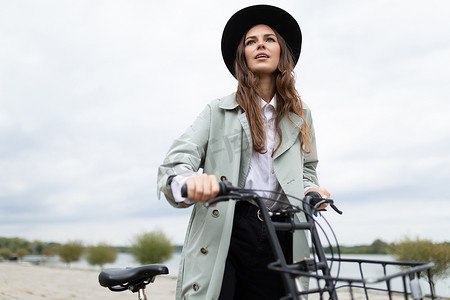 穿着雨衣和帽子的年轻时尚女性沿着海滨长廊骑自行车