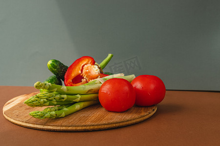 木板上放着蔬菜：西红柿、芦笋、黄瓜、红甜椒。