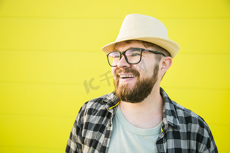 积极的年轻嬉皮士男子在黄墙商店户外背景上微笑的肖像 — 帅气的时髦胡子男子，戴着帽子和眼镜站在户外 — 时尚和时尚年轻人的概念