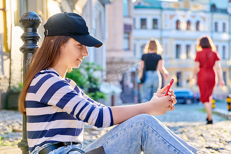都市风格、时尚少女坐在人行道上使用智能手机