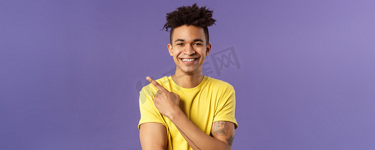 酷炫产品背景摄影照片_热情、快乐的年轻嬉皮士男性的特写肖像，带着恐惧、笑容满面、手指左上角，展示酷炫的产品，介绍一些非常好的紫色背景