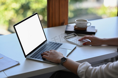 女会计师使用计算器并在办公桌上使用笔记本电脑。