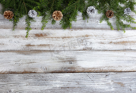 圣诞节或新年的银色和金色松果装饰品的顶部边框，在白色质朴的木材上配有真正的冷杉树枝
