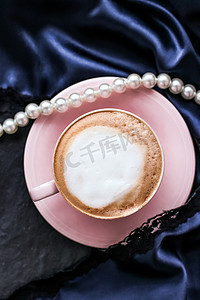珠宝背景摄影照片_一杯卡布奇诺早餐，配有缎子和珍珠珠宝背景，巴黎咖啡馆的有机咖啡和无乳糖牛奶，适合豪华复古度假品牌