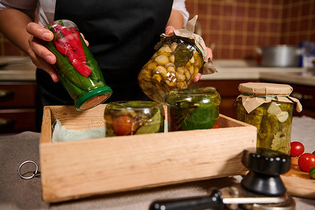 详细信息：家庭主妇手中装有罐装辣椒荚和腌制蘑菇的罐子。