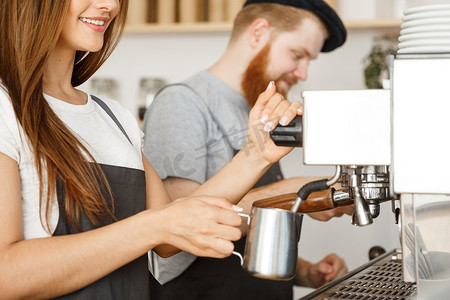 咖啡经营理念-穿着围裙的女咖啡师站在咖啡馆里与她的伙伴一起准备和蒸牛奶以订购咖啡的肖像。