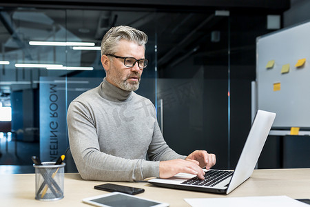 资深且经验丰富的程序员在现代办公室的笔记本电脑上工作，戴眼镜的男性网页设计师开发人员编写代码程序新应用程序，成熟的商人在办公桌前工作