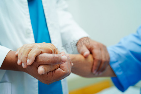 医生手牵亚洲老年女病人的手，在医院提供帮助和护理。