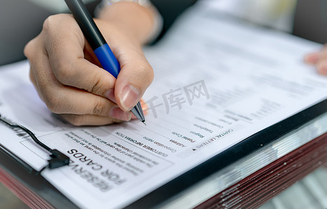 商务人员手持笔，以纸质形式填写公司简介以签订合同协议，并完成交易。