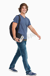 背着背包走路时拿着书的男学生