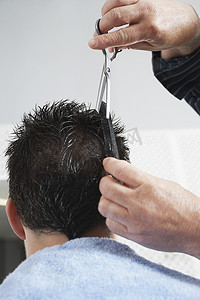 剪头发摄影照片_理发店里理发师给男人剪头发的特写