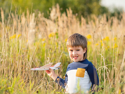 可爱的小孩在田野里玩玩具飞机。