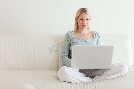 女人盘腿坐在沙发上，手里拿着笔记本