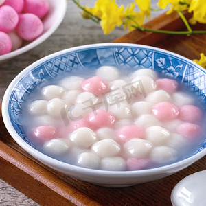 将红白相间的汤圆（汤圆，糯米饺子球）装在蓝色碗里，用木制背景做为冬至食品.