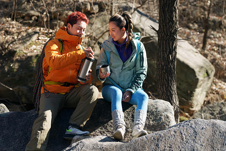 旅行水杯摄影照片_徒步旅行的青年伴侣坐在石头上休息