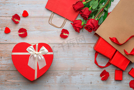 红色购物袋，装有情人的礼物，心形包装盒，木制表面的玫瑰和花瓣。情人节2月14日或浪漫的夜晚准备工作、明信片、海报、装饰品