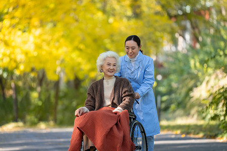 轮椅治疗摄影照片_护士推着坐在轮椅上的老人散步