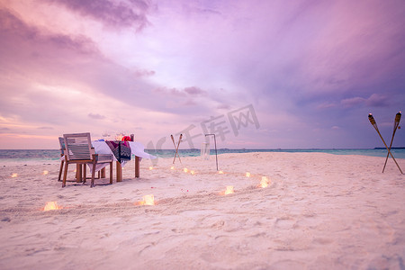 沙滩布置摄影照片_令人惊奇的浪漫晚餐在沙滩上的木制甲板与蜡烛下日落的天空。浪漫和爱情，奢华的目的地晚餐，异国情调的餐桌布置，海景尽收眼底