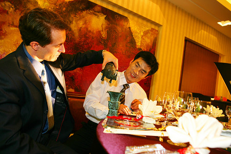 中外商务人士坐在酒店餐桌旁把玩工艺品
