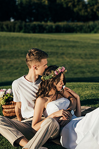 英俊的新郎拥抱美丽的新娘婚纱礼服和花圈野餐 