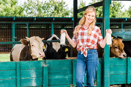 cow摄影照片_beautiful farmer showing bottles of cow milk near stable 