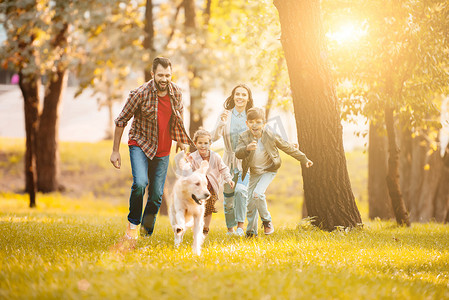 在公园里与金猎犬一起奔跑的微笑的夫妇和孩子的前面看法 
