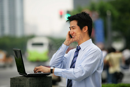 上海浦东写字楼旁一位男商务人士使用笔记本电脑时打手机