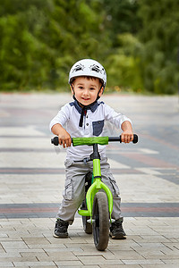 儿童男孩骑在他头戴头盔的第一辆自行车上的白色头盔。没有踏板的自行车.