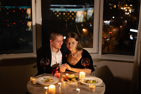 两人的浪漫晚餐，点着蜡烛，烛光与美酒约会，情侣在情人节恋爱，男人和女人在家里共度感情假期，2月14日庆祝的理念