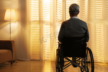 老人烦恼摄影照片_窗前孤独的老年人坐在轮椅上